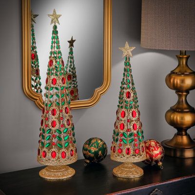 three christmas trees sitting on top of a wooden table next to a mirror and lamp