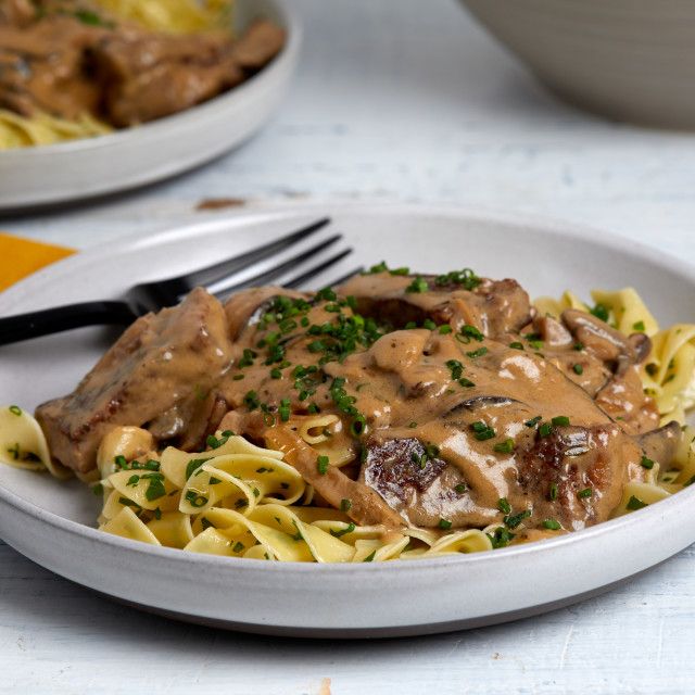 a white plate topped with pasta and meat covered in gravy next to a fork