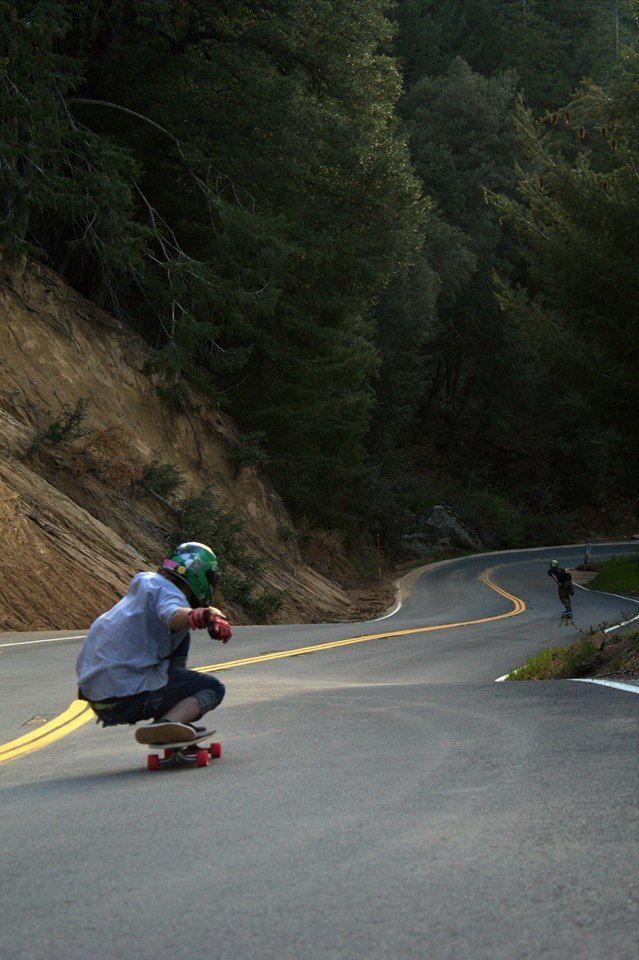 a man riding a skateboard down a curvy road next to a forest