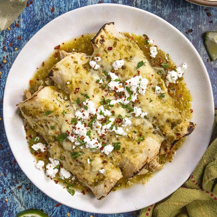 a white plate topped with fish covered in feta cheese and green sauce next to sliced limes