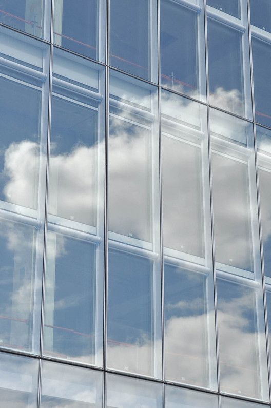 an airplane is flying in front of a glass building with clouds reflected in the windows