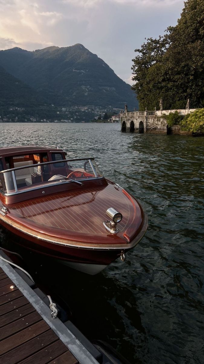 a small wooden boat docked at a pier on the water with mountains in the background