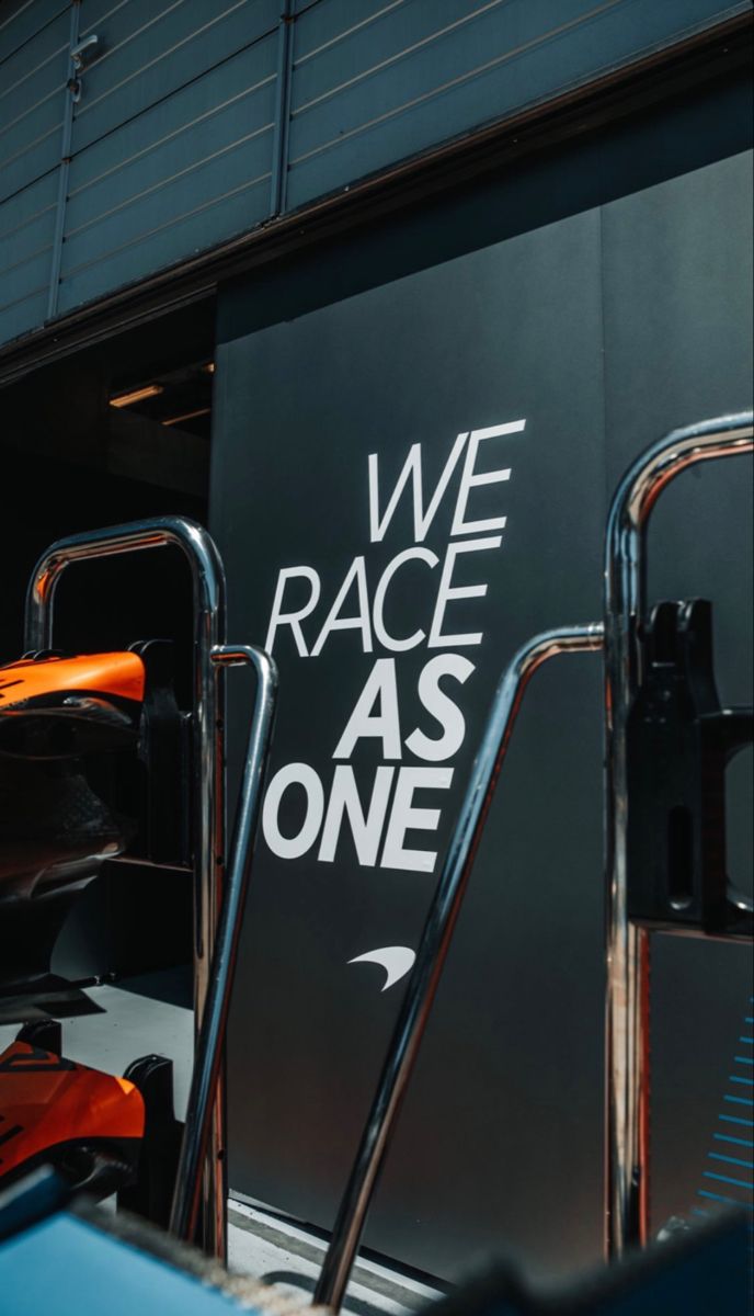 an orange and black race car parked in front of a sign that says we race as one