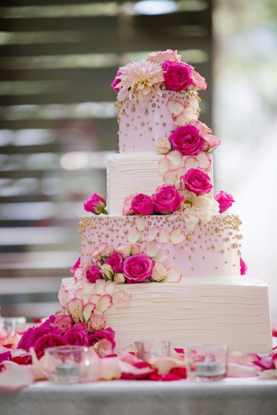 a wedding cake with pink and white flowers on the top is surrounded by other desserts