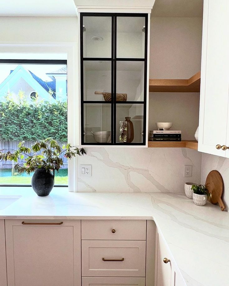 a kitchen with white cabinets and marble counter tops, potted plants on the window sill