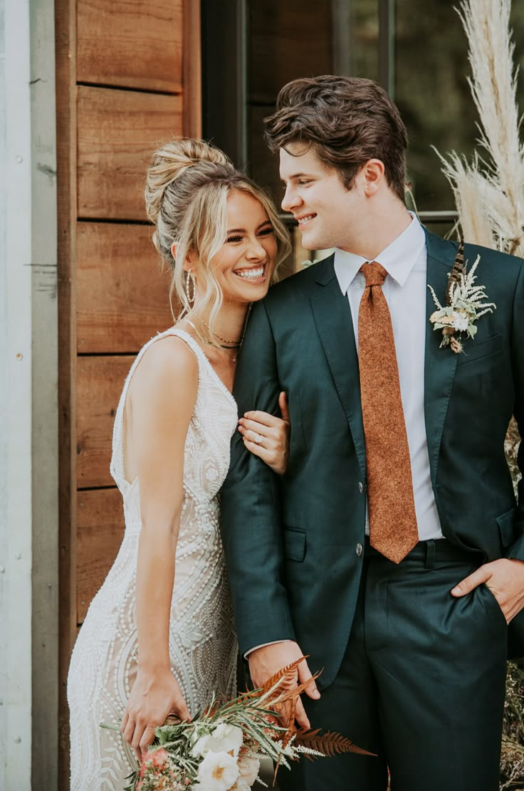 a bride and groom standing next to each other in front of a building with tall grass