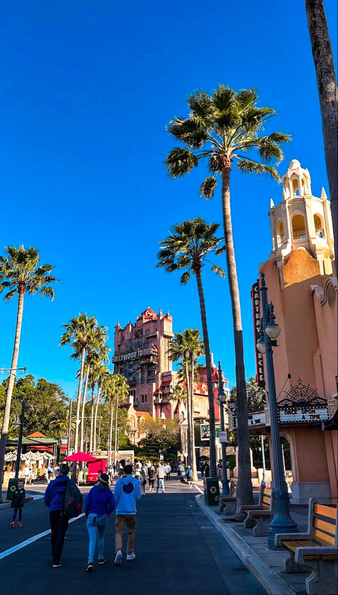 people walking down the street in front of buildings and palm trees on a sunny day