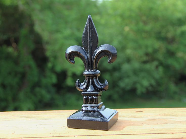 a metal fleur de lis on top of a wooden table next to trees