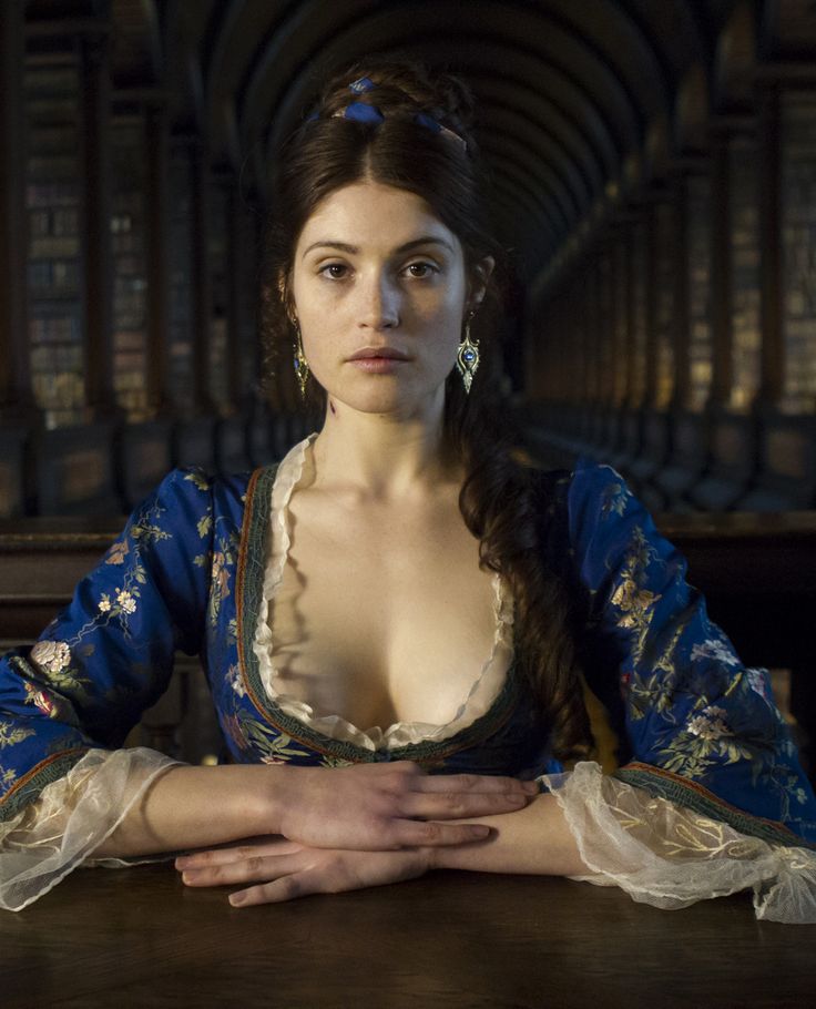 a woman sitting at a table in front of bookshelves with her hands on her chest