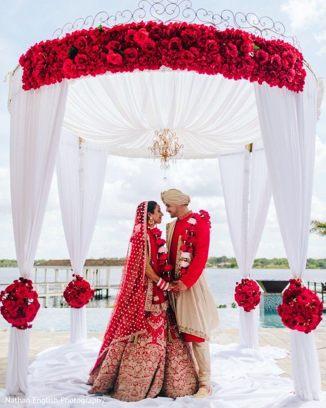 a newly married couple standing under a canopy with red flowers