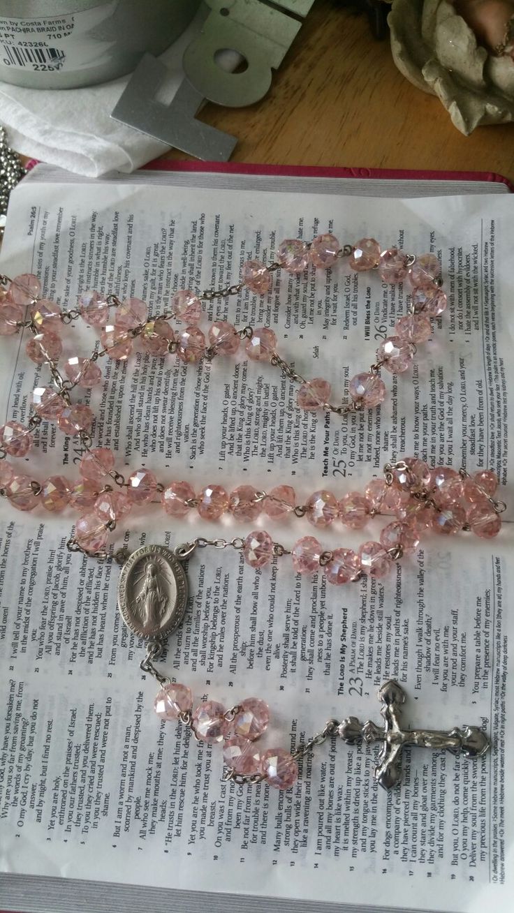 a rosary with pink beads and a crucifix is on top of an open book