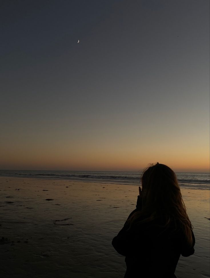 a woman standing on top of a sandy beach next to the ocean at night time