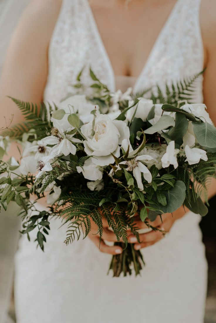 a bride holding a bouquet of white flowers and greenery