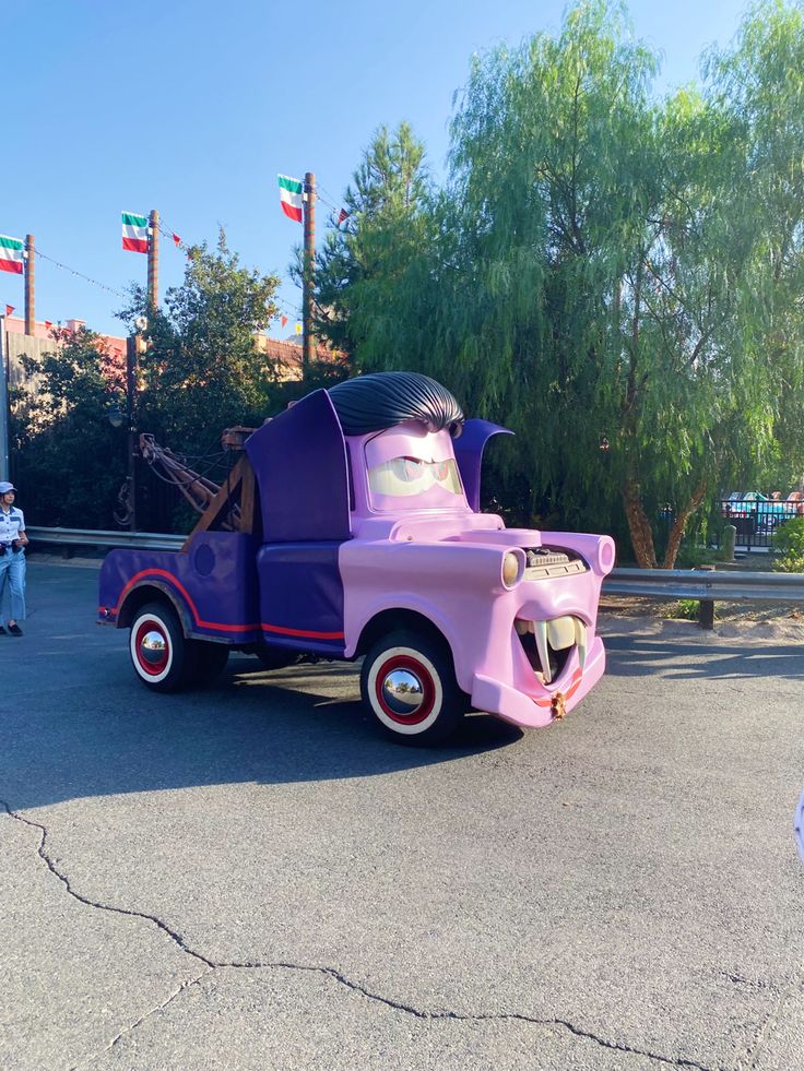 a pink and purple truck with a guitar on the back in a parking lot next to trees