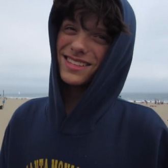 a young man wearing a blue hoodie standing in front of the beach and ocean