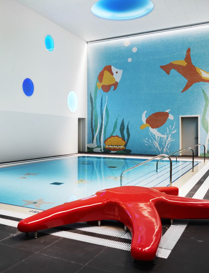 an indoor swimming pool with fish painted on the walls and floor, along with red chairs