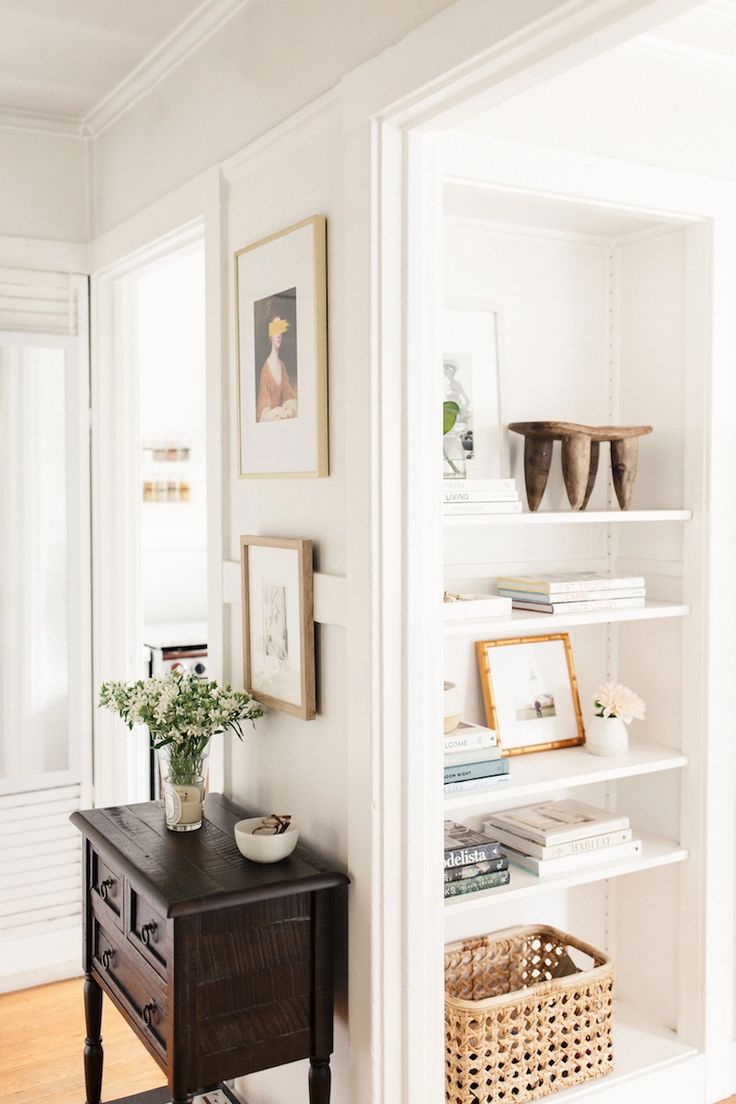 a room with white walls and shelves filled with books, vases and pictures on the wall