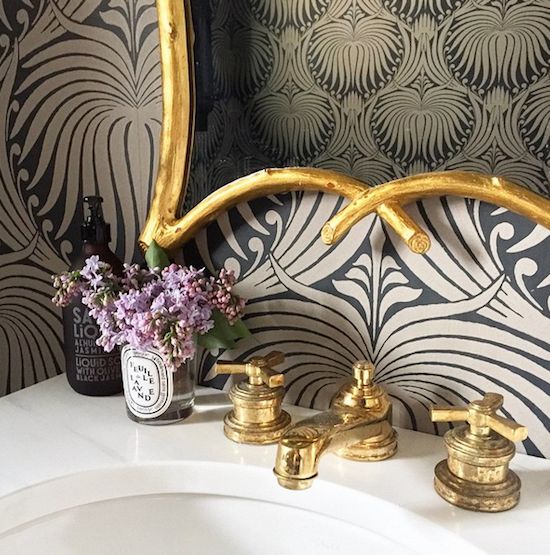 a bathroom sink with two faucets and a mirror above it that is decorated in black and gold