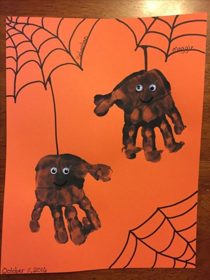 two handprints are hanging from a spider web on an orange paper with black eyes