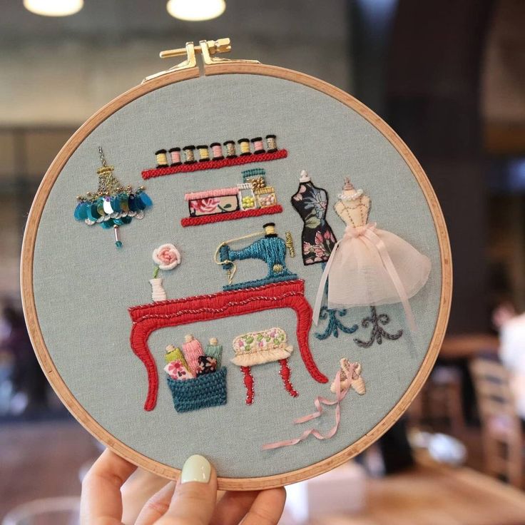 a person holding up a embroidery hoop with various items on it in front of a table