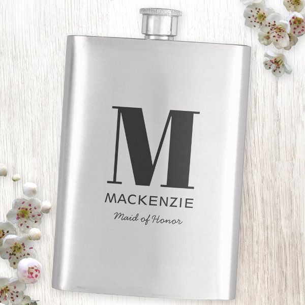 a stainless steel flask with the letter m on it and flowers in the background