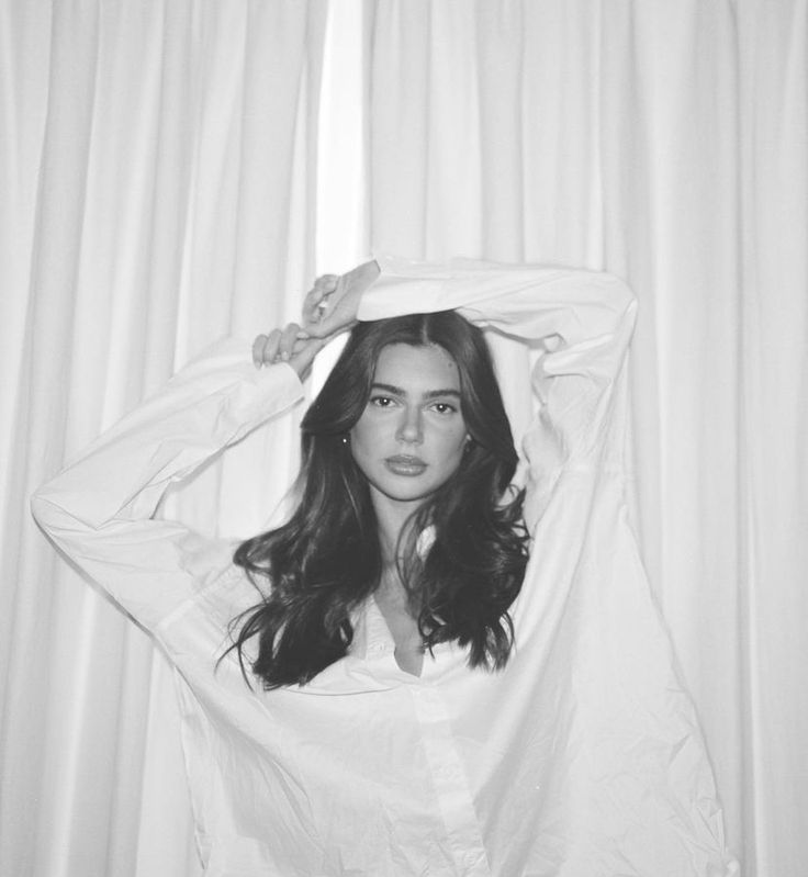 a woman standing in front of a curtain with her hands on her head and looking at the camera