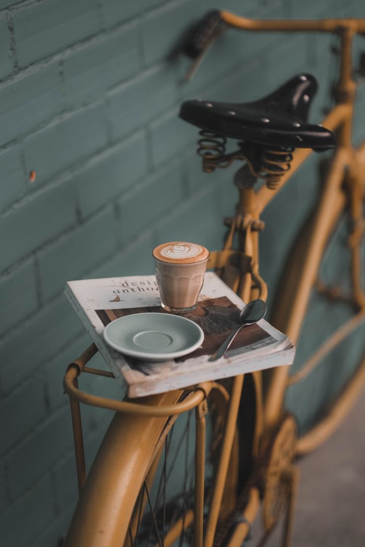 a bicycle parked next to a brick wall with a cup of coffee on the front