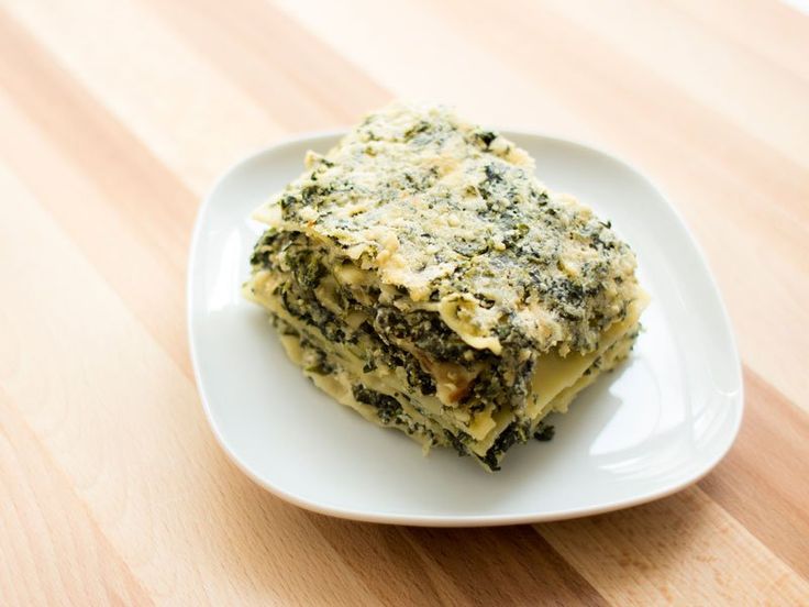 a white plate topped with lasagna covered in cheese and spinach toppings