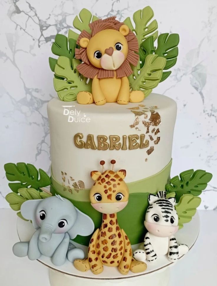 a three tiered cake decorated with jungle animals and a lion on top, surrounded by green leaves