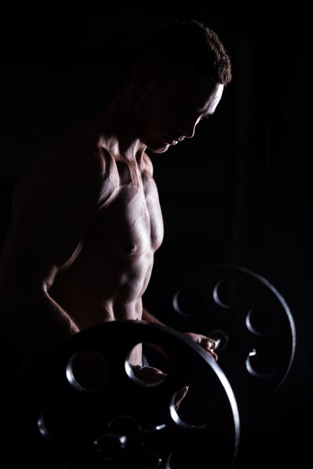 a shirtless man lifting a barbell in the dark with his hands on his hips