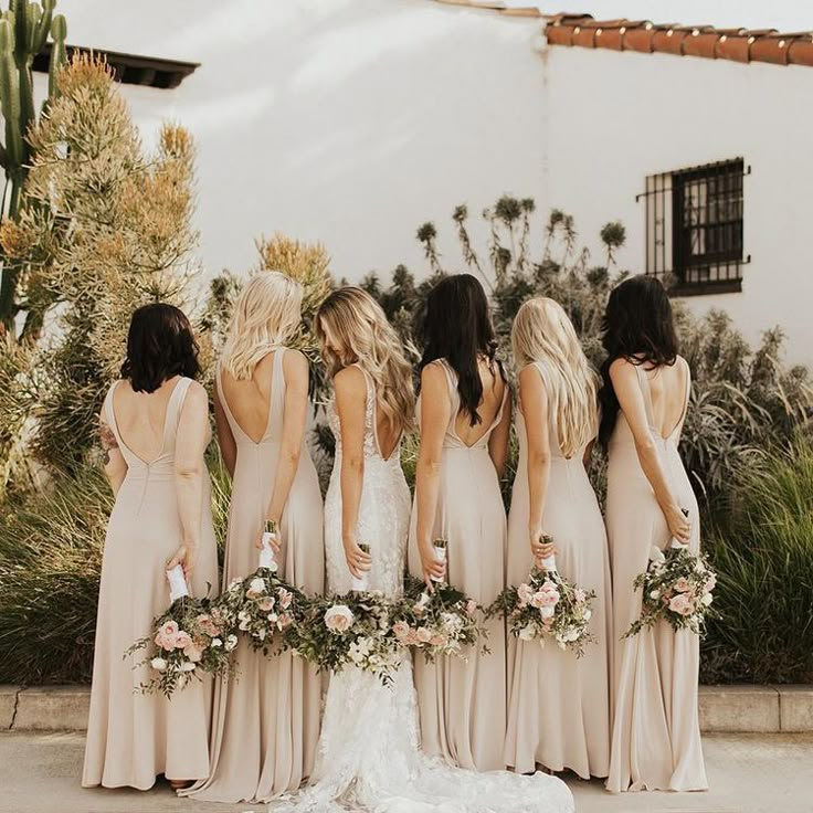 a group of women standing next to each other in long dresses and holding bouquets