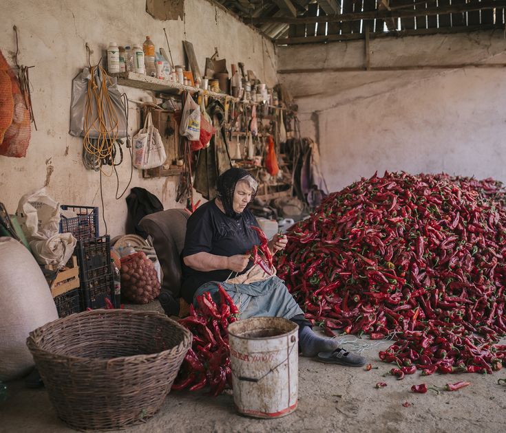 a woman sitting in front of a pile of red peppers