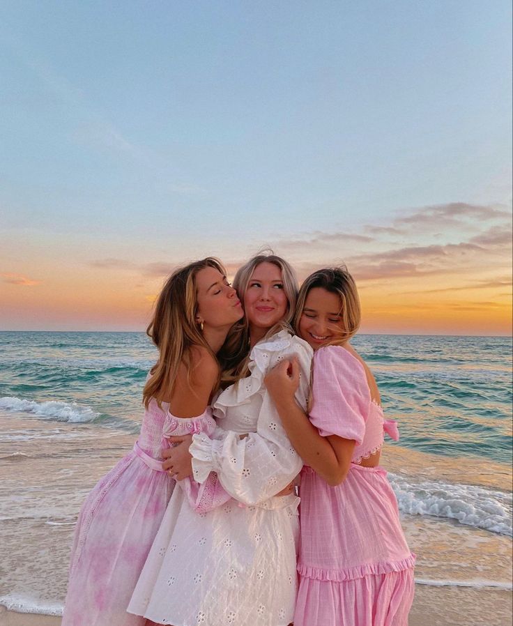 three girls in dresses hugging on the beach