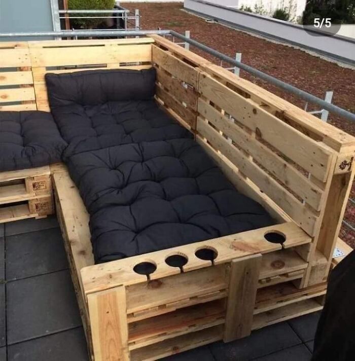 a couch made out of wooden pallets on top of a roof with black cushions