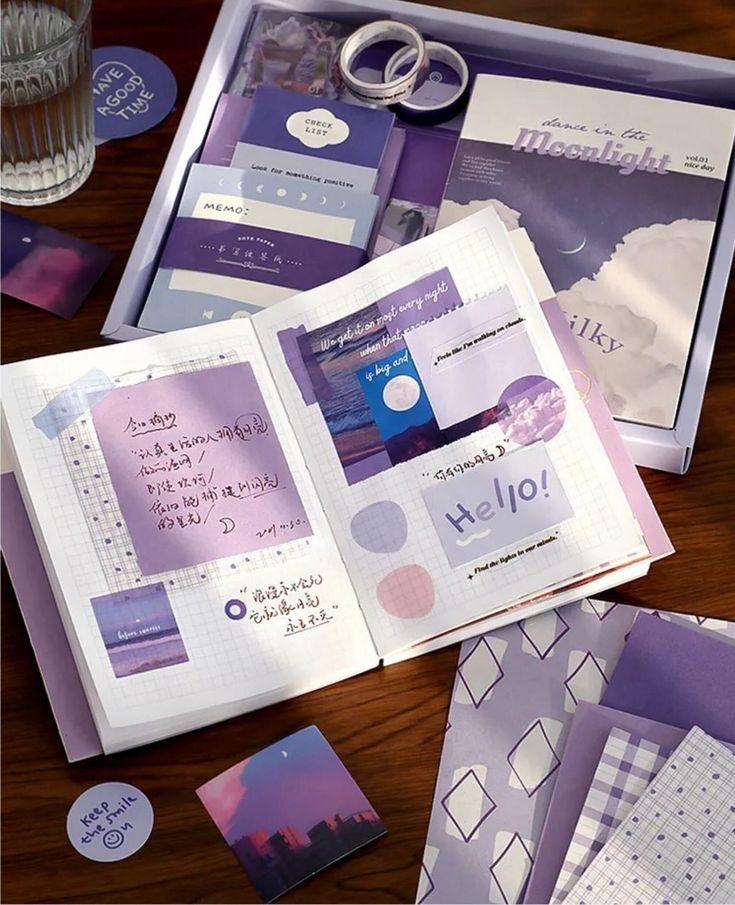 an open book on a wooden table with purple and white papers, scissors and other items