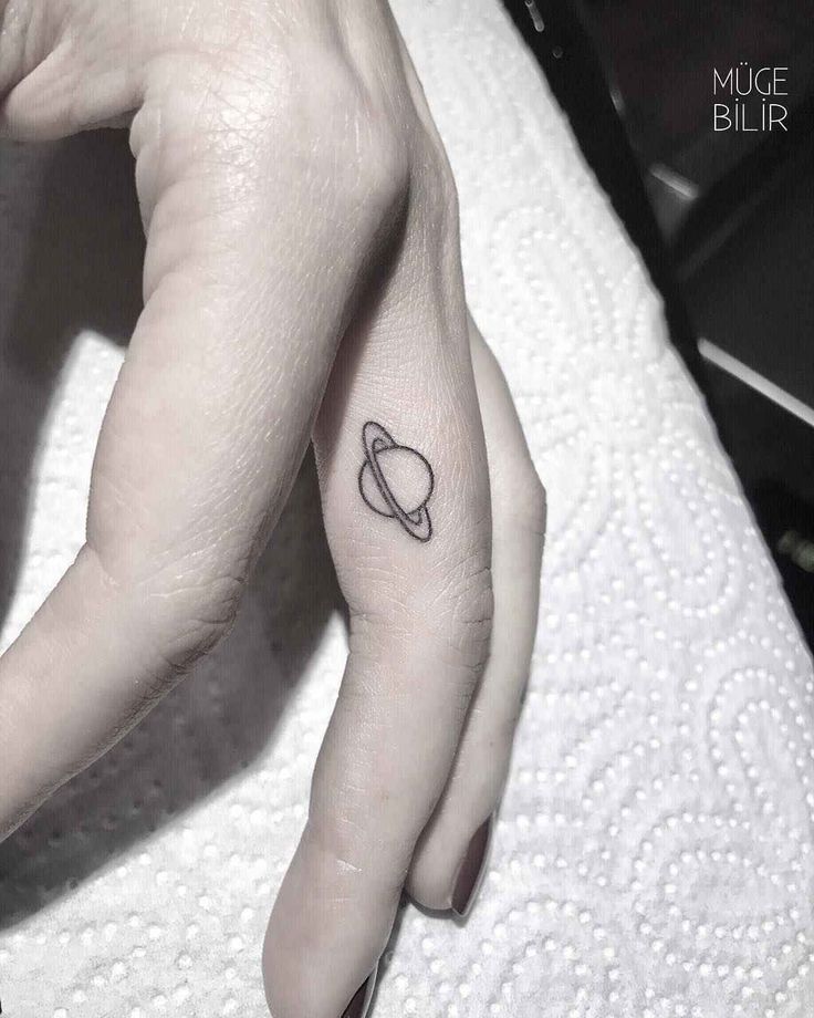 a small saturn tattoo on the left side of the hand, with an arrow in it