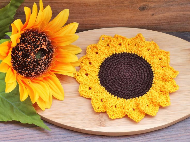 two crocheted sunflowers sitting on top of a wooden plate next to each other