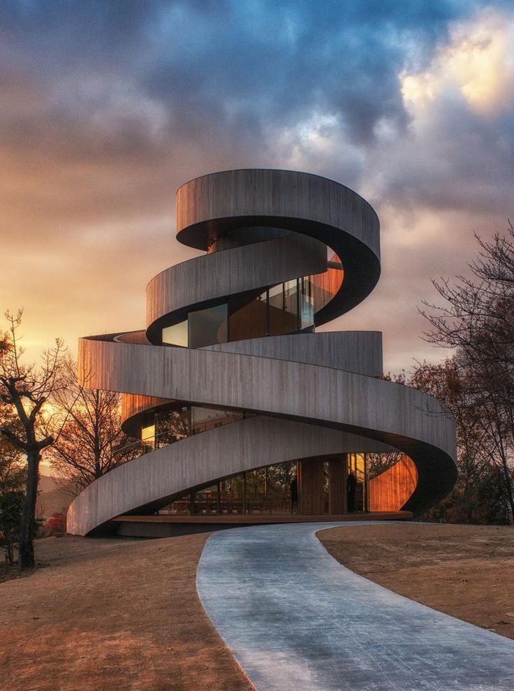 a spiral shaped building in the middle of a field with trees and clouds behind it