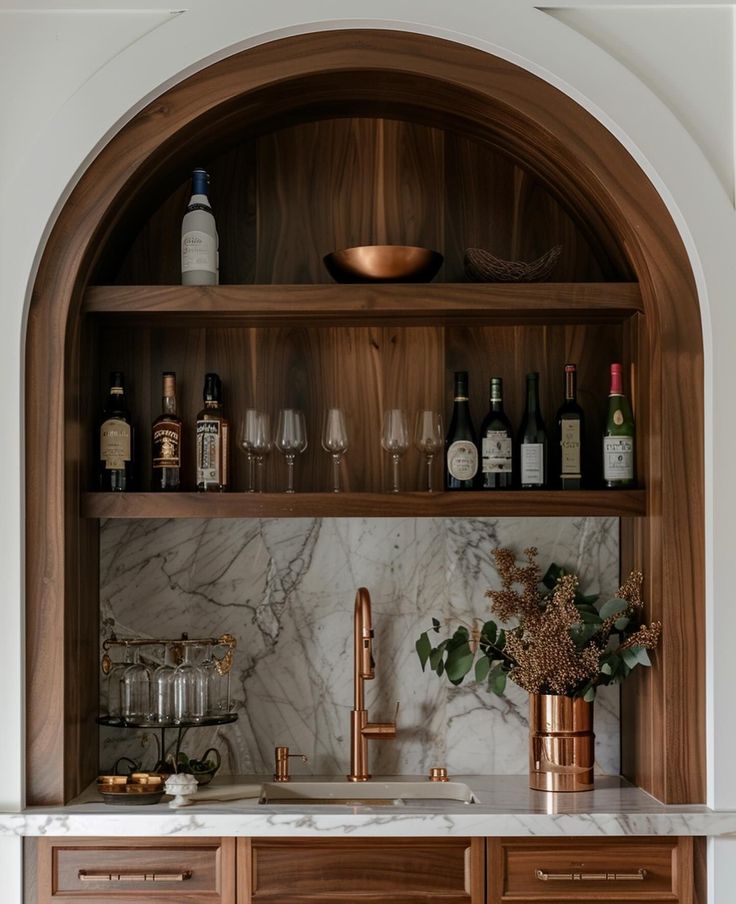 a kitchen with marble counter tops and wooden cabinets, wine glasses on the shelf above the sink