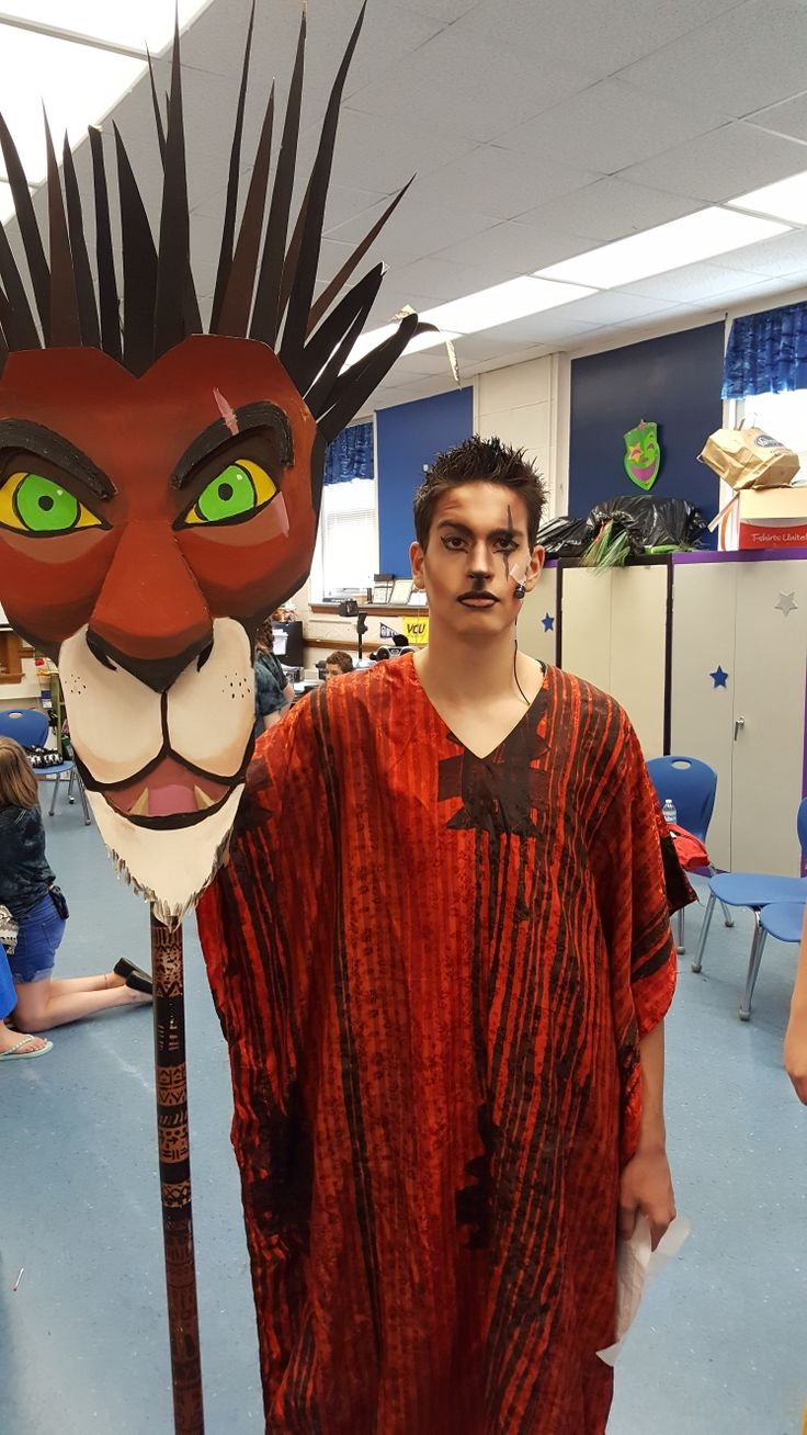 a man standing next to a lion mask on top of a wooden pole in a room