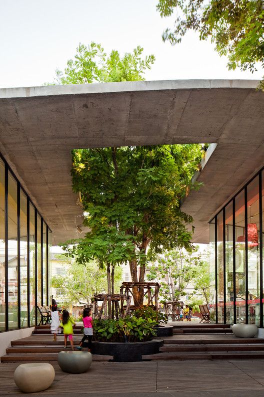 two children are walking in front of a building with glass walls and trees on the outside