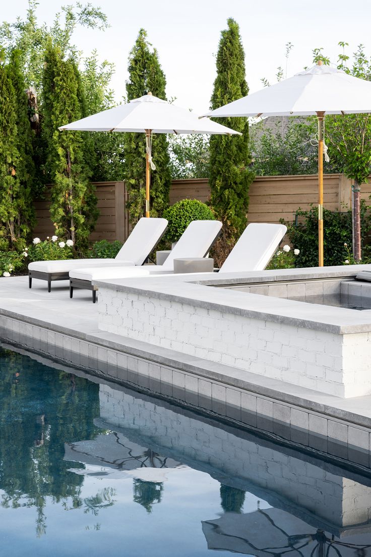 an outdoor pool with lounge chairs and umbrellas next to the side of the pool