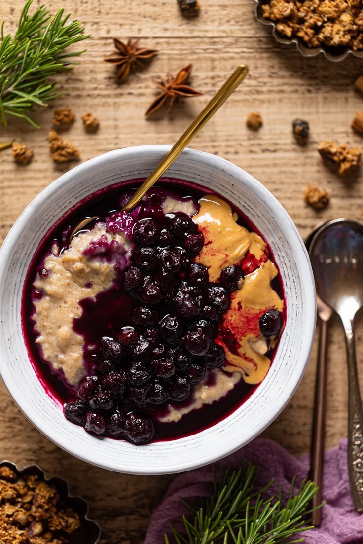 a bowl of oatmeal with blueberries and honey on the side next to spoons