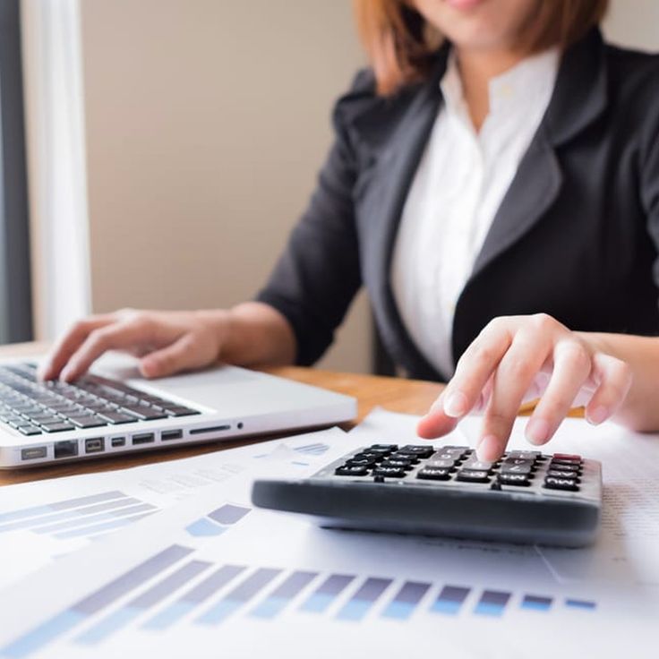 a woman is typing on a calculator in front of a laptop and papers