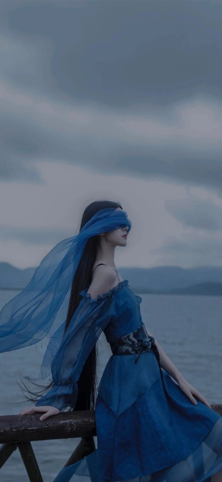 a woman in a blue dress standing on a pier