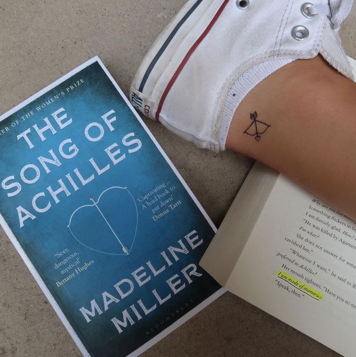 a person's arm with a tattoo on it next to a book titled the song of achilles