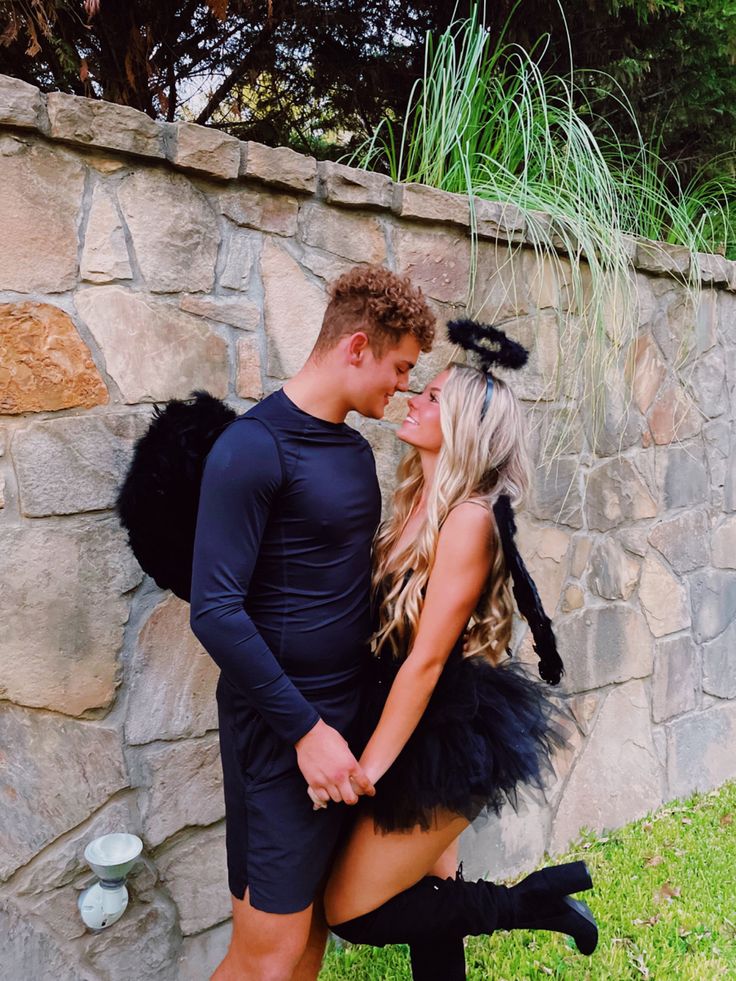 a man and woman dressed up in costumes standing next to a stone wall with grass