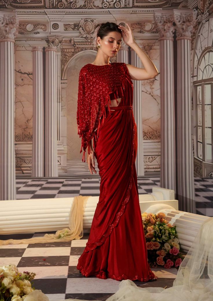 Capture attention in this striking red crepe sari, featuring a beautifully embroidered border that adds a touch of sophistication to its elegant silhouette. The ensemble is paired with a plain padded blouse adorned with asymmetrical capes, each embellished with exquisite embroidery and finished with long tassels for added flair. Completing the look is a stylish belt that cinches the waist, making this outfit perfect for any festive occasion where you want to make a memorable statement. Tuxedo Accessories, Beach Wedding Guests, Ritu Kumar, Jacket Cape, Gown Skirt, Padded Blouse, Hand Accessories, Beach Bride, Embroidered Border