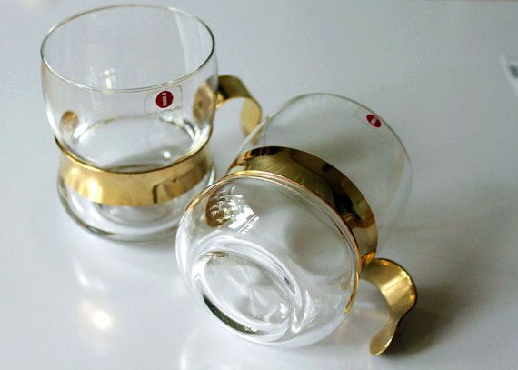 two glass cups sitting next to each other on a white counter top with gold trimmings