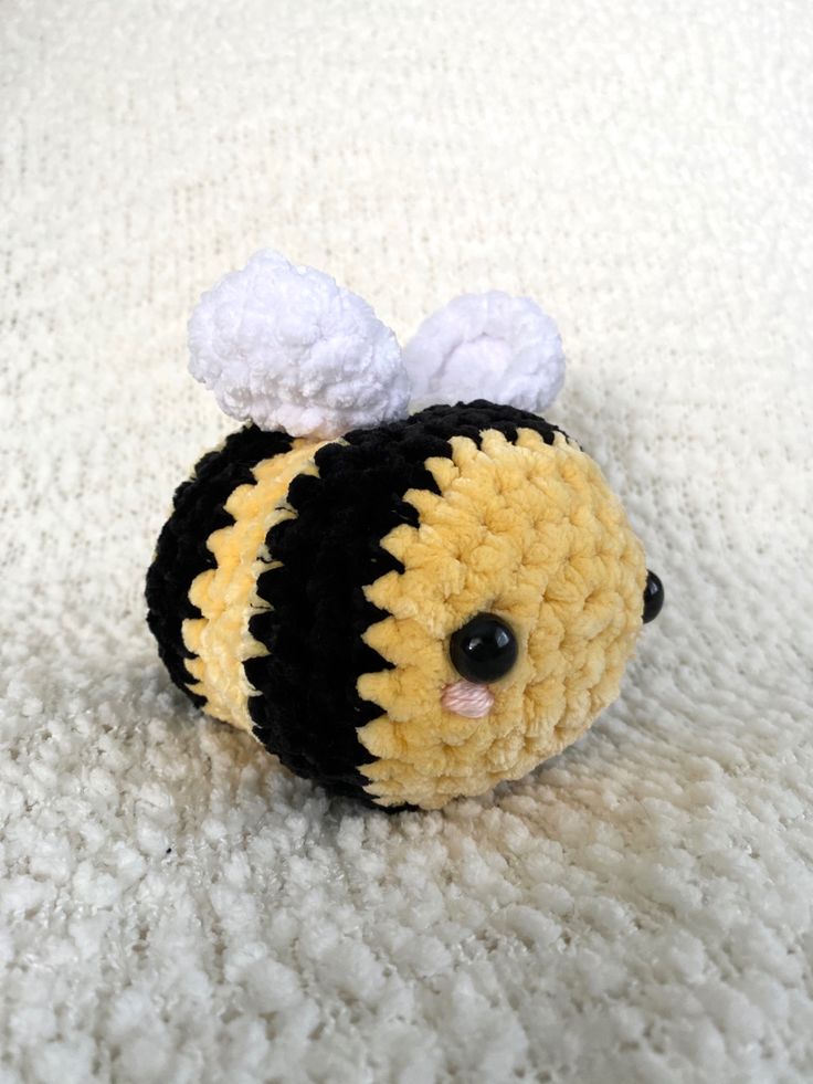 a yellow and black crocheted stuffed animal on a white blanket with one eye open